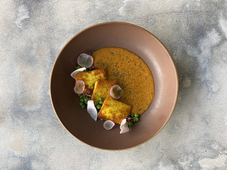 Delicious Indian curry served with crispy fried tofu, garnished with radish slices, green peas, and edible flower petals for a colorful presentation.