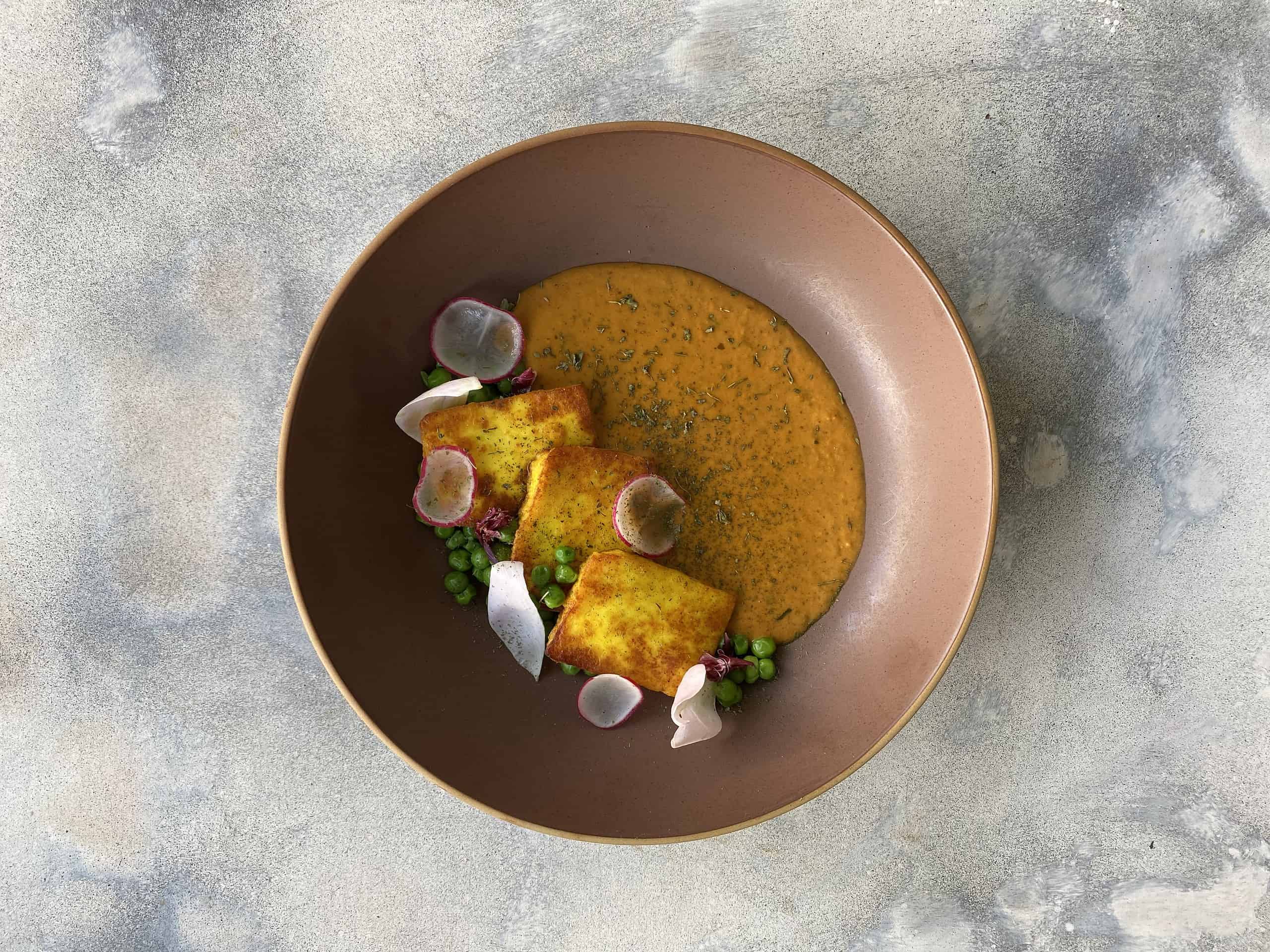 Delicious Indian curry served with crispy fried tofu, garnished with radish slices, green peas, and edible flower petals for a colorful presentation.