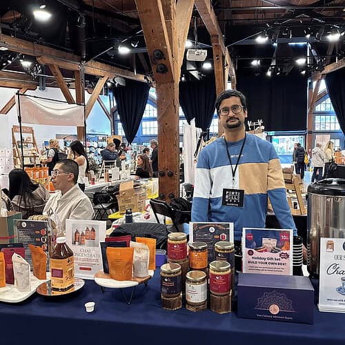 Bright indoor marketplace featuring Indian spices, teas, and food products with a vendor showcasing traditional chai blends at The Indian Pantry event.