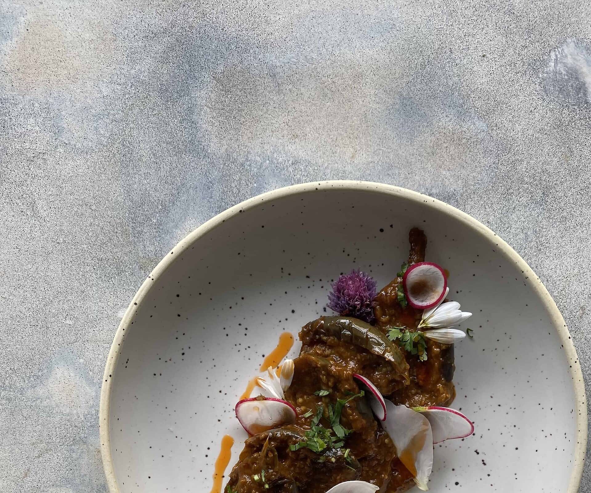 Rich Indian cuisine featuring flavorful eggplant curry with garnishes of radish slices and edible flowers, perfect for authentic Indian food lovers.